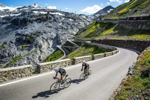 Dwóch kolarzy pokonuje serpentyny na przełęczy Stelvio, otoczeni surowym, górskim krajobrazem.