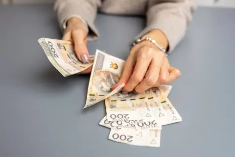 Dłonie liczą banknoty 200 zł, przygotowując świadczenie urlopowe.