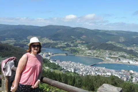 Mujer con sombrero blanco y blusa rosa posa en el mirador de San Roque, disfrutando de la vista panorámica de la ría y el pueblo.