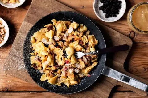 Kaiserschmarrn-Rezepte: Ein goldbrauner Kaiserschmarrn mit Mandelsplittern, Rosinen und Apfelstücken in einer Pfanne, bestäubt mit Puderzucker.