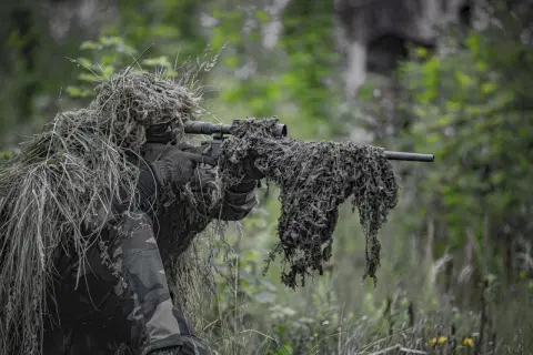 Un francotirador camuflado en un bosque, listo para la acción. El airsoft, un deporte que simula combates, requiere sigilo y estrategia.
