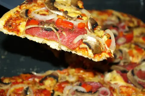 Kawałek pysznej pizzy salami z pieczarkami i cebulą, unoszący się nad resztą zapiekanki.