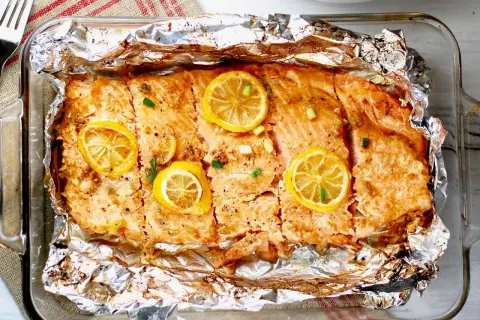 Pyszny, pieczony filet z łososia z plasterkami cytryny i szczypiorkiem, podany w folii aluminiowej.