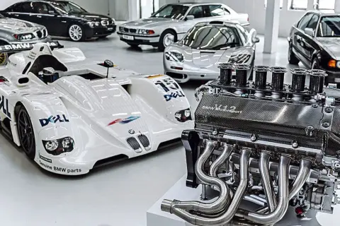 Silnik V12 BMW Motorsport obok białego bolidu wyścigowego i kilku klasycznych BMW.