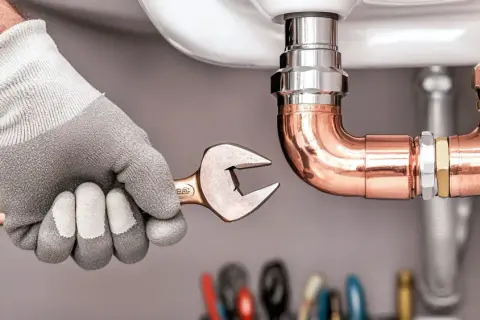 Hand mit Handschuh und Schraubenschlüssel arbeitet an Kupferrohren. Ein Projekt zur wasserleitung selbst verlegen wird hier gezeigt.