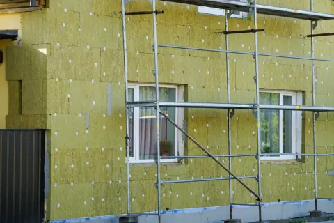 Dom ocieplany najlepszą wełną mineralną. Widać rusztowanie i okna.