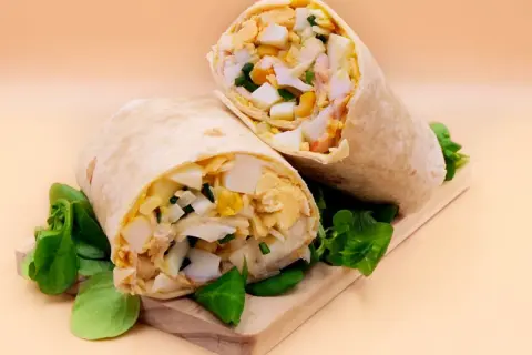 Pyszna tortilla z jajkiem, warzywami i kurczakiem, podana na desce z zieloną sałatą. Idealna na szybki lunch.