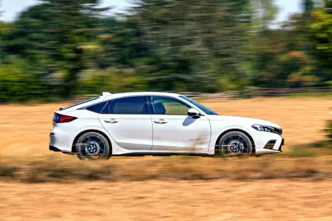 Biały Honda Civic 2025 pędzi przez suche pole, zostawiając za sobą smugi kurzu i rozmazane drzewa.