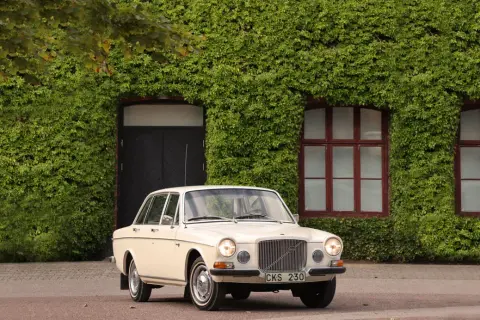 En klassisk Volvo 164 från 1973 parkerad framför en vackert klätterväxttäckt byggnad.