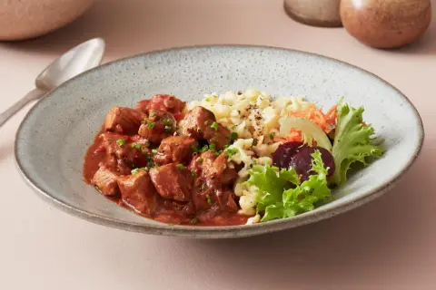 Herzhaftes ungarisches Gulasch mit Nockerln als Beilage, garniert mit frischem Salat und Rote Bete.