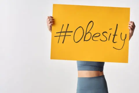 Osoba trzymająca tabliczkę z napisem #Obesity. Problem otyłości w Polsce staje się coraz poważniejszy.
