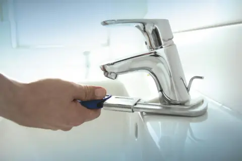 Mano con chiave per cambiare rubinetto lavandino bagno.
