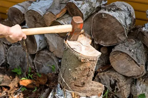 Holz spalten mit Axt. Auch wenn es nass wird, darf Brennholz so gelagert werden, bis es trocken ist.