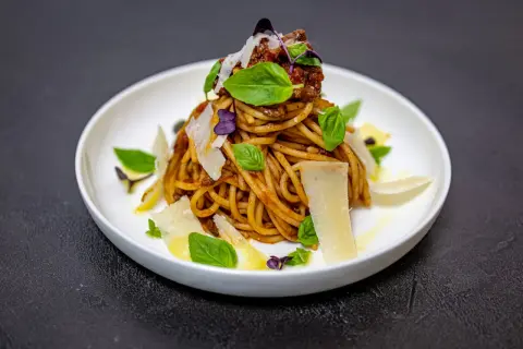 Pyszne spaghetti alla norma z sosem pomidorowym, bakłażanem, bazylią i parmezanem, podane na białym talerzu.