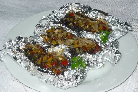 Kaszanka z grilla z cebulą i warzywami, zapieczona w folii aluminiowej, podana na białym talerzu.