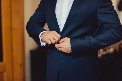 Mężczyzna zapina elegancki, granatowy **strój formalny**. Widać białą koszulę i mankiet z francuskimi spinkami.