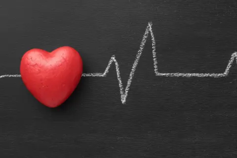 Cuore rosso su lavagna nera con tracciato ECG. Un simbolo di cosa fa alzare la pressione.