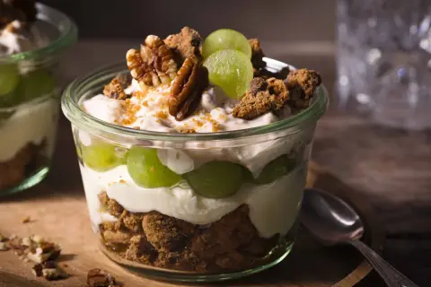 Cremiges Dessert im Glas mit grünen Trauben, zerbröselten Keksen und Nüssen. Ein köstlicher Trauben-Cookie-Dessert-Genuss.