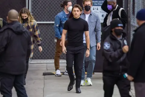 Tom Holland indossa un outfit elegante con scarpe perfette per pantaloni a sigaretta donna, mentre cammina con un gruppo di persone.