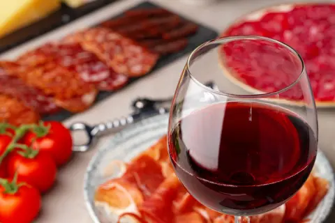 Glas Rotwein neben Aufschnitt und Tomaten. Ein Fest für Genießer, das den Unterschied Portwein Sherry erahnen lässt.