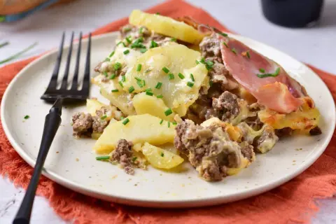 Zapiekanka ziemniaczana z mięsem mielonym, posypana szczypiorkiem, na talerzu z widelcem.