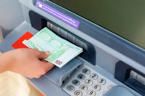 Ręka odbiera banknoty 100 euro z bankomatu PKO.