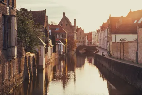 En kanal i Brygge, Belgien, med gamla tegelhus och en bro. Solen går ner och reflekteras i vattnet.