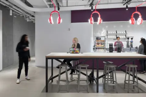 Inside Spotify Studios NYC, people gather around a communal table, with iconic headphone lights overhead.
