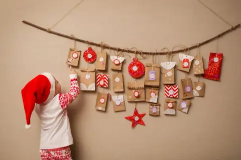 Dziecko w czapce Mikołaja wybiera prezent z kalendarza adwentowego dla dzieci pomysły. Zawieszony na gałęzi, pełen małych paczuszek z numerami.