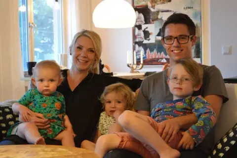 Famille souriante, avec deux enfants sur les genoux des parents. Le nom de famille suédois est Johansson.