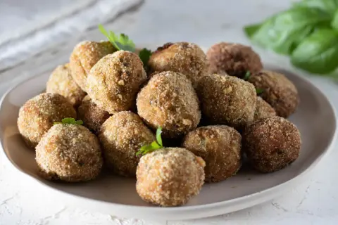 Un piatto colmo di polpette di melanzane, dorate e croccanti, pronte per essere gustate. La ricetta originale che conquista tutti.