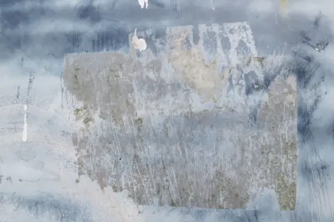 Texture de papier peint foncé avec des traces de colle à enlever, révélant des zones plus claires et des éraflures.