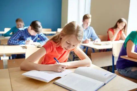 Uczniowie piszą w zeszytach, zastanawiając się, ile wynosi stypendium szkolne.