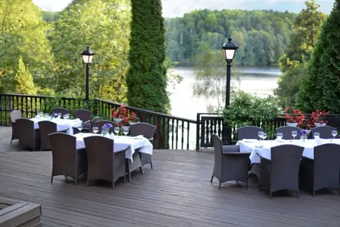 Elegancki taras z nakrytymi stołami i widokiem na jezioro. Idealne miejsce na relaks w spa na Mazurach.