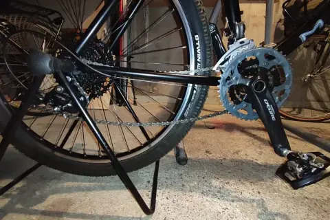 Widok tylnego koła i korby roweru. Pokazuje mechanizm przerzutek i łańcuch, który można naciągnąć, aby rower działał płynnie.
