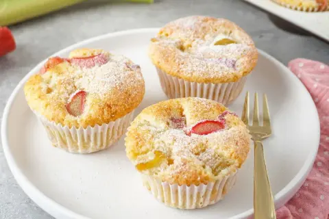 Saftige rhabarber muffins mit joghurt, bestäubt mit Puderzucker, auf einem Teller mit einer goldenen Gabel.