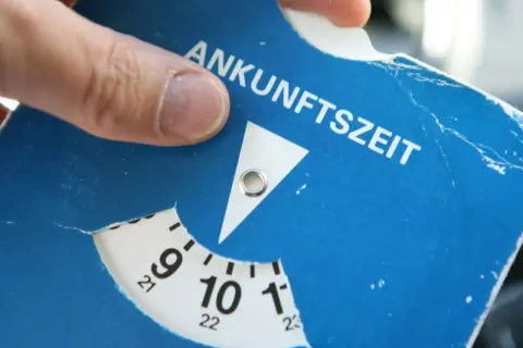 Ein Finger dreht die Scheibe einer Parkscheibe, um die Ankunftszeit einzustellen. So funktioniert eine Parkuhr: Zeit einstellen, auslegen, fertig.