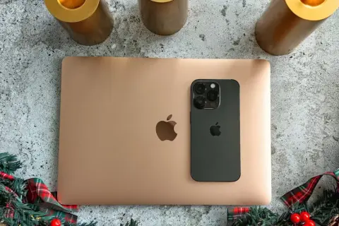 Złoty MacBook i czarny iPhone na tle świątecznych dekoracji. Idealny zestaw do pracy i rozrywki z macOS.
