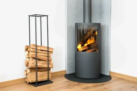 Stufa moderna con fiamme vive e legna accatastata in un elegante porta legna, per un accogliente riscaldamento a legna.