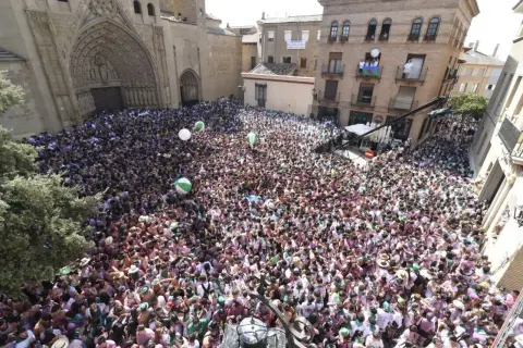 Multitud celebra en la plaza de Huesca, con globos verdes y blancos flotando. La fiesta prelaurentis inunda las calles.