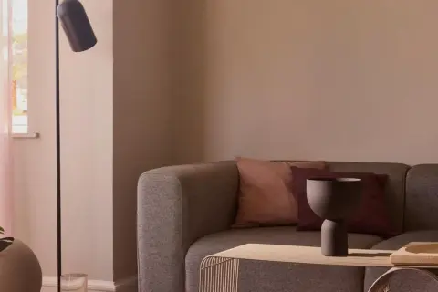 Gemütliches Sofa mit Kissen in mauve farbe, daneben ein moderner Stehlampenfuß und ein Fenster mit zarten Vorhängen.