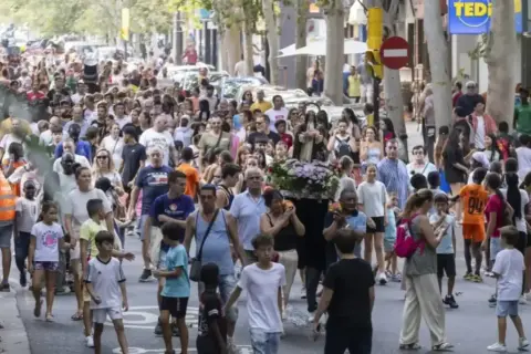 Multitud celebra las fiestas del barrio Las Fuentes en Zaragoza. Una procesión avanza por la calle con gente de todas las edades.