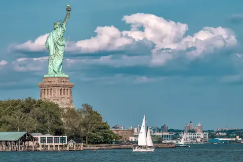 Statua Wolności i żaglówka na wodzie. Zastanawiasz się, ile kosztuje lot do USA z Polski?