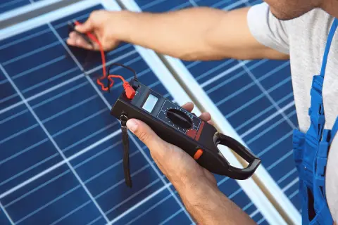 Technik sprawdza panel fotowoltaiczny miernikiem. To kluczowy element, który zamienia prąd stały na zmienny, czyli co to jest falownik fotowoltaiczny.
