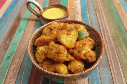 Beignets de choux-fleurs dorés et croustillants, servis dans un bol en terre cuite avec une sauce jaune crémeuse. Parfaits pour un apéritif savoureux.
