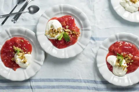 Tre vita skålar med rabarberkompott kardemumma, toppad med grädde och nötter. En härlig dessert.