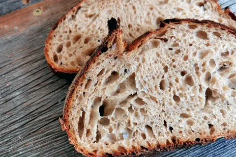 Zwei Scheiben rustikales Sauerteigbrot mit knuspriger Kruste und luftiger Krume liegen auf einem Holzbrett. Ein gesundes Frühstück!