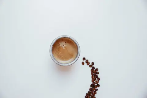 Un caffè pregiato, con la sua crema invitante, accanto a chicchi tostati su sfondo bianco.