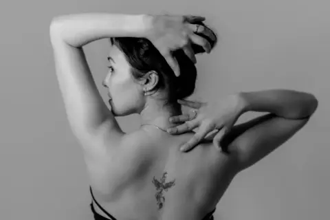 Rückenansicht einer Frau mit einem Phönix-Tattoo, einem der beliebten Tattoos. Ihre Hände sind im Haar und am Nacken.
