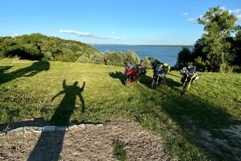 Trzy motocykle na wzgórzu z widokiem na jezioro i las.